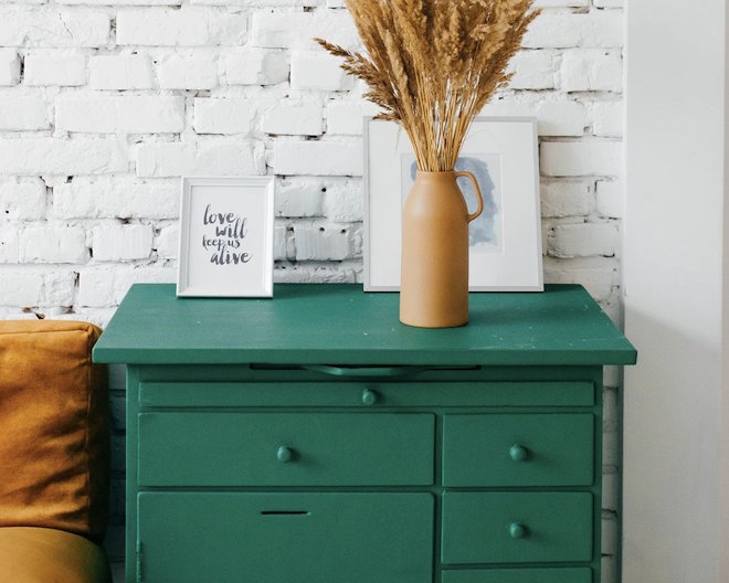 Terra cotta vase holding dried spikes and two picture frames on top of a green dresser