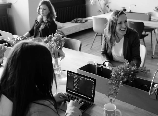 Three women working on computers around table.